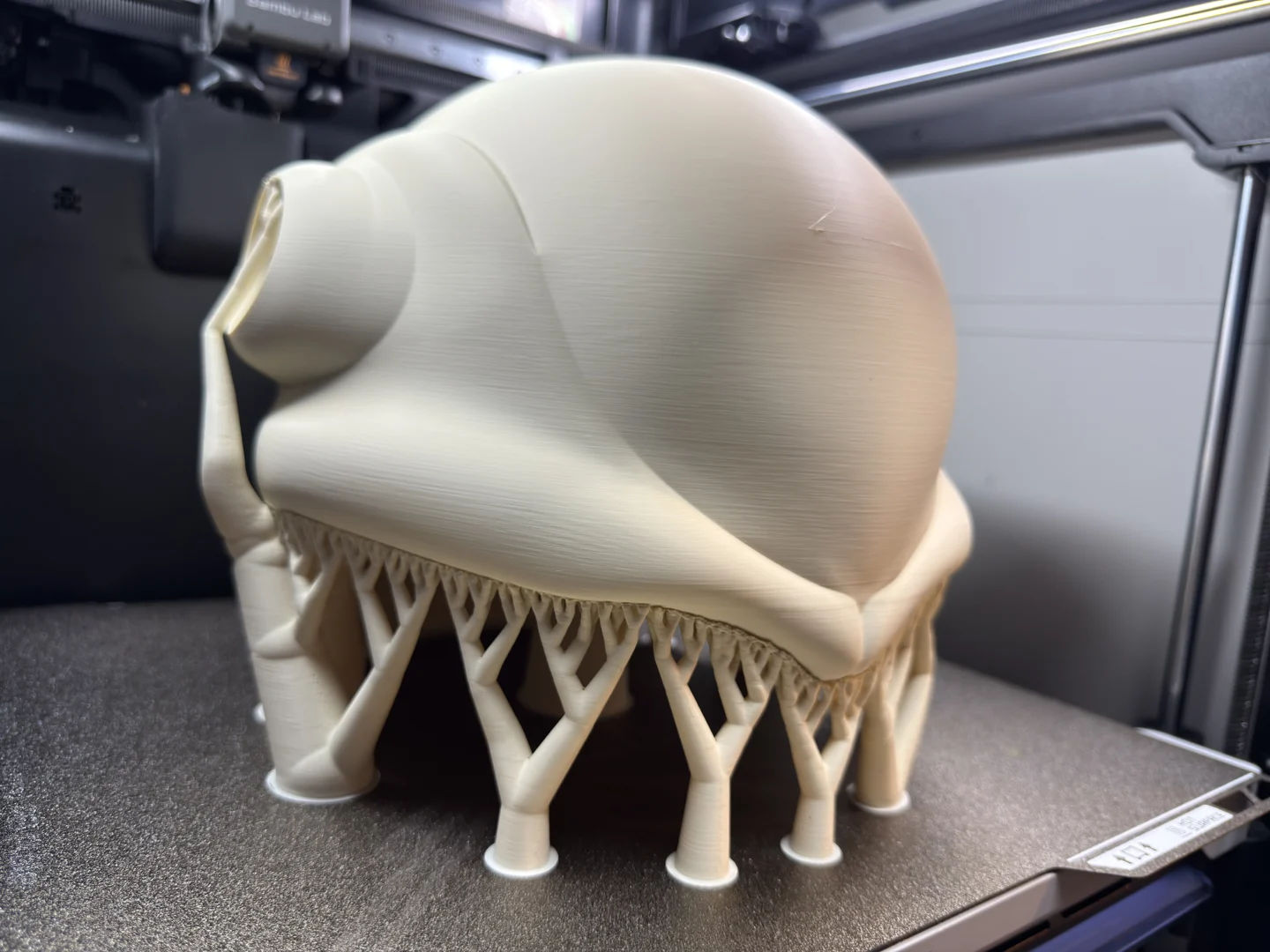 Raw cream-coloured Frieza helmet on the printer bed with tree supports beneath the rim